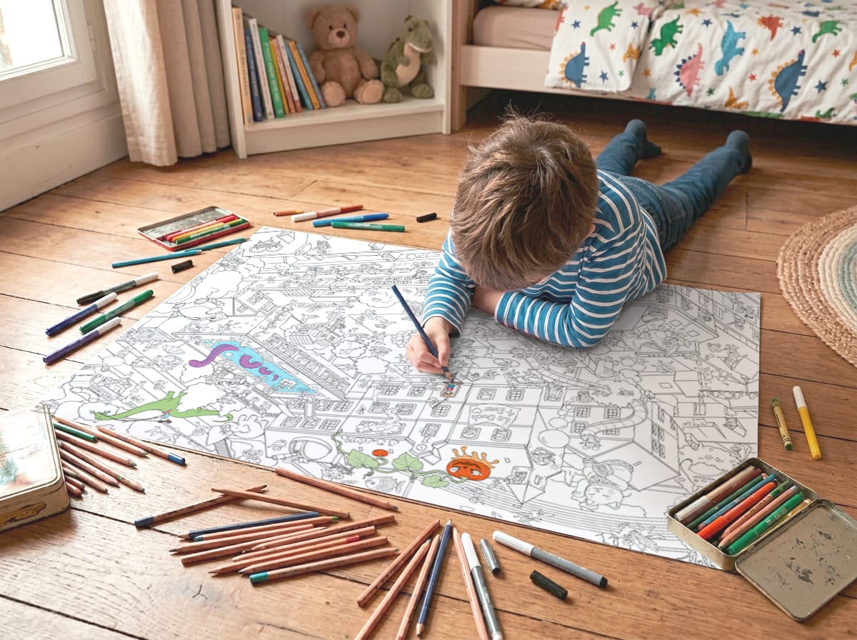 Un enfant allongé sur le sol de sa chambre colorie le poster géant, entouré de feutres et de crayons de couleur